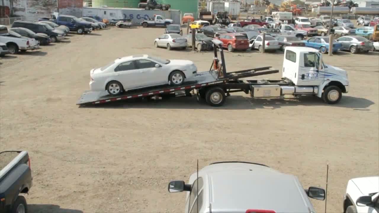 TNT Towing flatbed loading a vehicle in a salvage lot full of cars